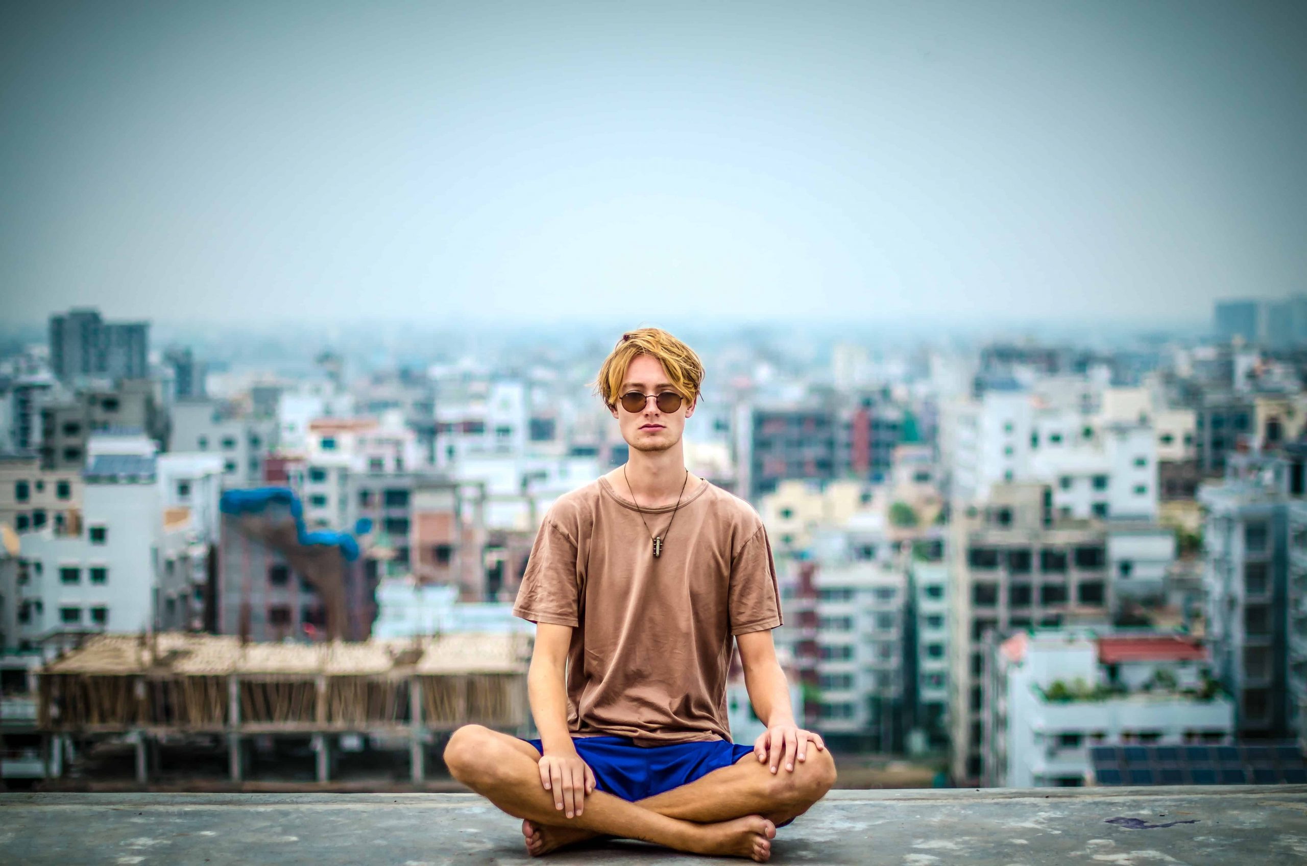 Man sitting cross legged with city landscape behind him.